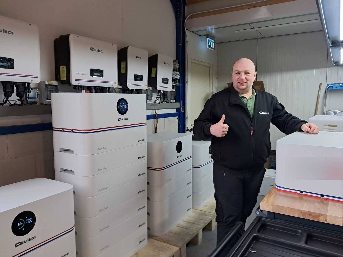 Collega van Altilia steekt zijn duim op tussen thuisbatterijen en omvormers in de testruimte