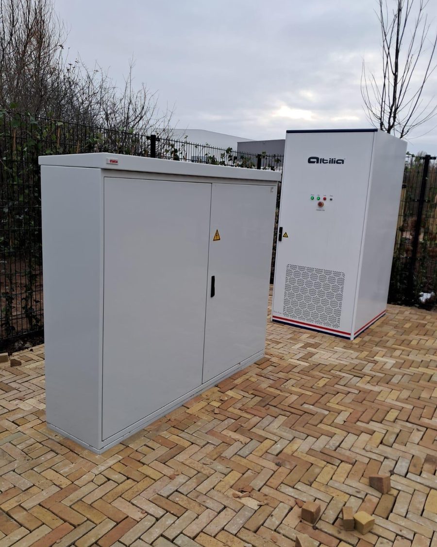Vloeistofgekoelde Altilia energiekast op een bedrijfsterrein met klinkers, naast een grijze verdeelkast